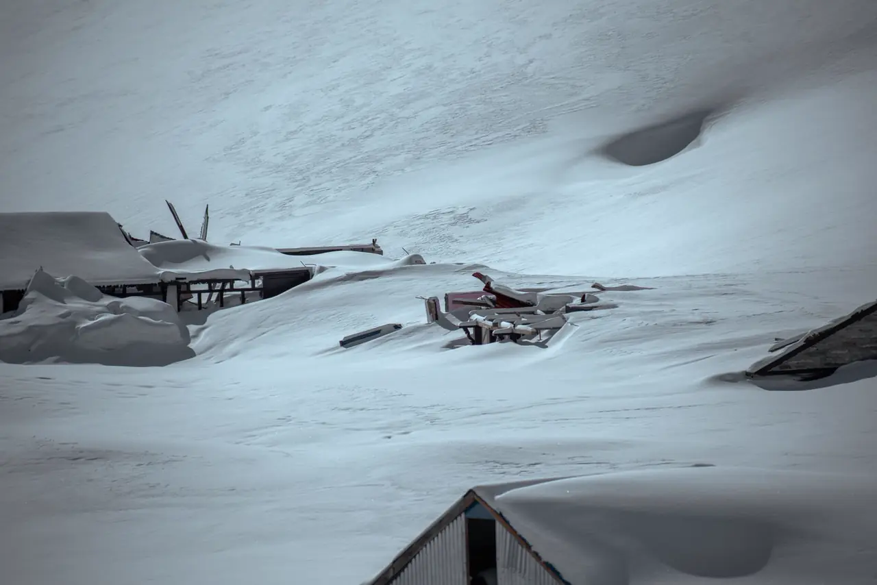Touring skis and skins leaning against a timber lodge wall in the snow.